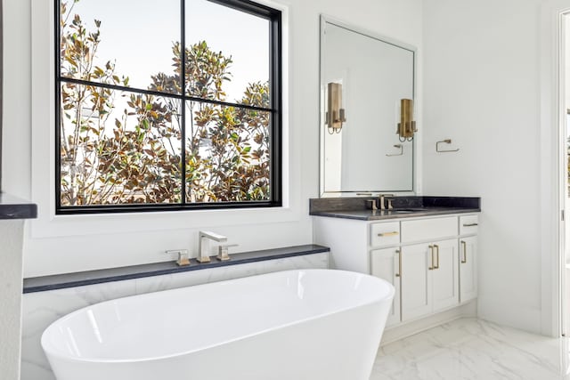 bathroom with marble finish floor, a freestanding tub, vanity, and a healthy amount of sunlight