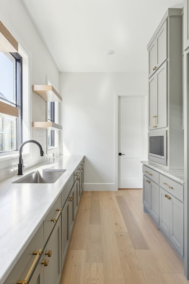 kitchen featuring light stone counters, gray cabinetry, a sink, built in microwave, and light wood finished floors