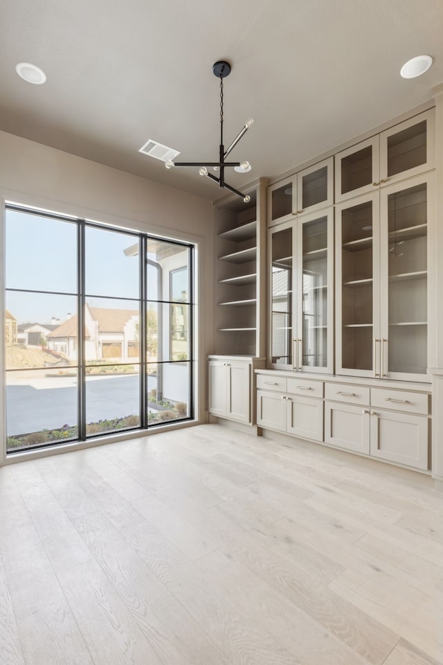 unfurnished living room with light wood-style flooring, a water view, visible vents, and a notable chandelier