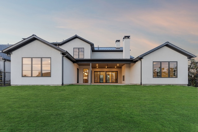 back of house at dusk with metal roof, a standing seam roof, a lawn, and stucco siding