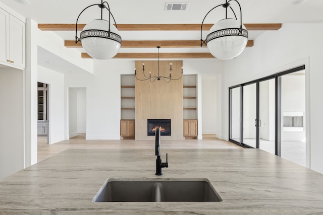 kitchen featuring decorative light fixtures, visible vents, a large fireplace, white cabinets, and a sink