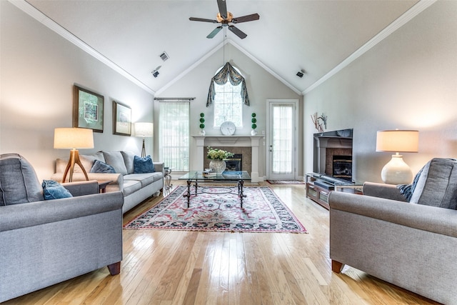 living room featuring a tile fireplace, ceiling fan, high vaulted ceiling, light wood-type flooring, and ornamental molding