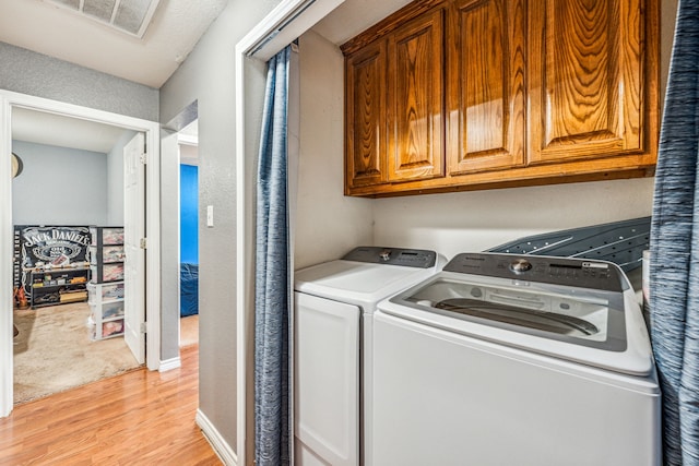 clothes washing area with washer and clothes dryer, light hardwood / wood-style floors, and cabinets