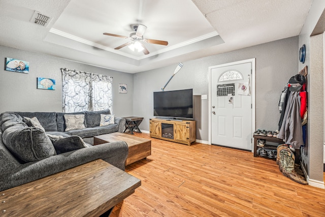 living room featuring ceiling fan, wood-type flooring, crown molding, and a tray ceiling