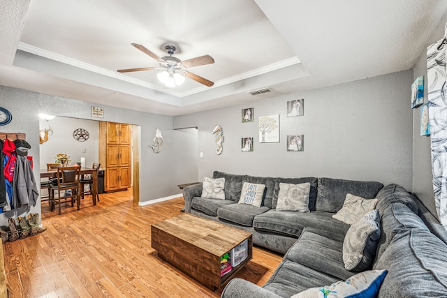 living room with a raised ceiling, ceiling fan, crown molding, and light hardwood / wood-style floors