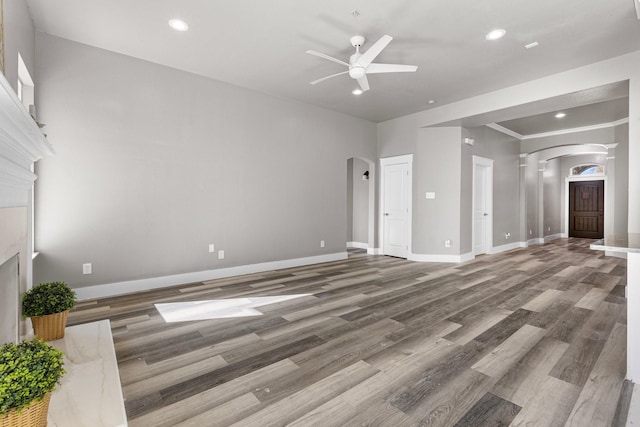 unfurnished living room featuring arched walkways, baseboards, ceiling fan, and wood finished floors