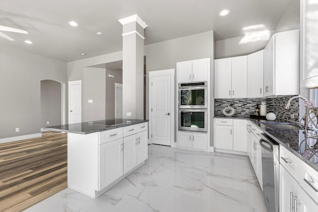 kitchen with arched walkways, a sink, decorative backsplash, stainless steel appliances, and marble finish floor