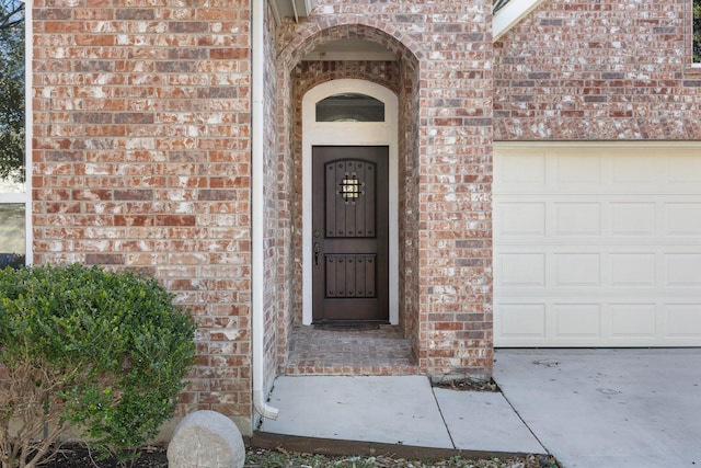 view of exterior entry with brick siding and an attached garage