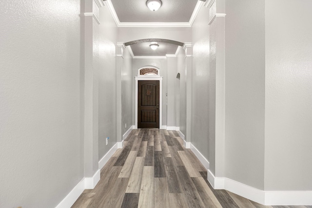 hallway with baseboards, wood finished floors, arched walkways, and ornamental molding