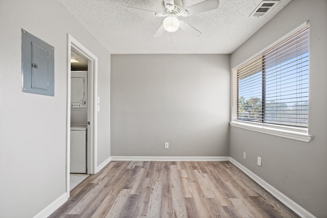 unfurnished room featuring a textured ceiling, electric panel, stacked washer / drying machine, and light hardwood / wood-style floors