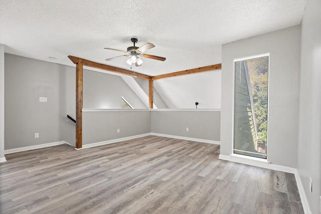 unfurnished room featuring vaulted ceiling with beams, light wood-type flooring, a textured ceiling, and ceiling fan