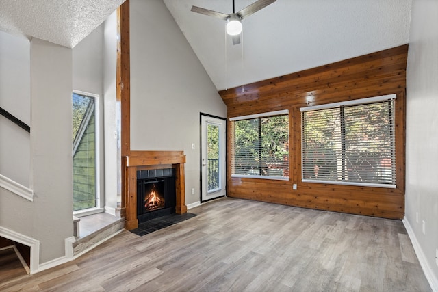 unfurnished living room with a healthy amount of sunlight, a textured ceiling, high vaulted ceiling, and a tiled fireplace