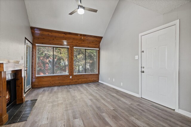 unfurnished living room featuring ceiling fan, dark wood-type flooring, high vaulted ceiling, wood walls, and a textured ceiling