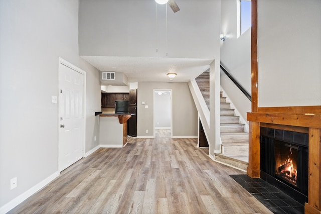 unfurnished living room with a tiled fireplace, ceiling fan, light hardwood / wood-style floors, and a high ceiling