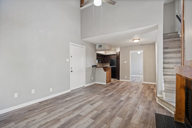 unfurnished living room with ceiling fan, a high ceiling, light hardwood / wood-style floors, a textured ceiling, and a fireplace