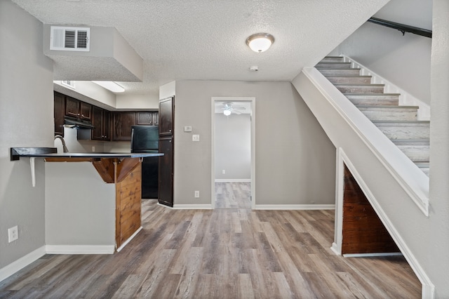 kitchen with a kitchen bar, a textured ceiling, light hardwood / wood-style floors, and dark brown cabinetry