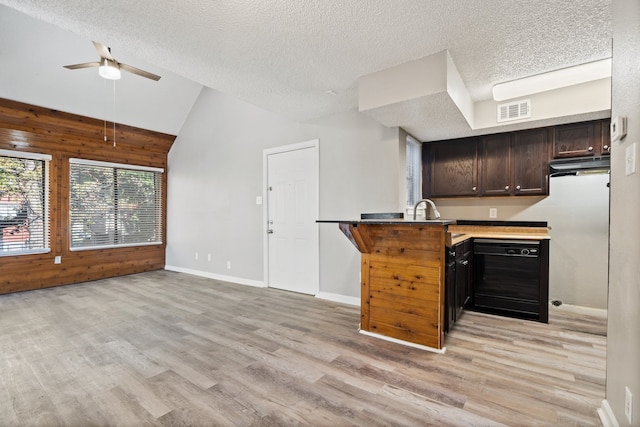 kitchen featuring kitchen peninsula, light wood-type flooring, vaulted ceiling, black dishwasher, and wood walls