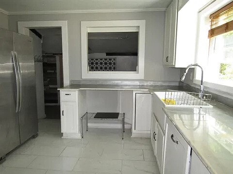 kitchen with white cabinetry, stainless steel fridge, and crown molding