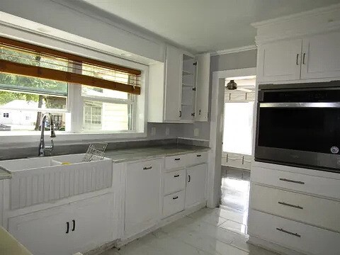 kitchen with white cabinets, sink, crown molding, and stainless steel oven