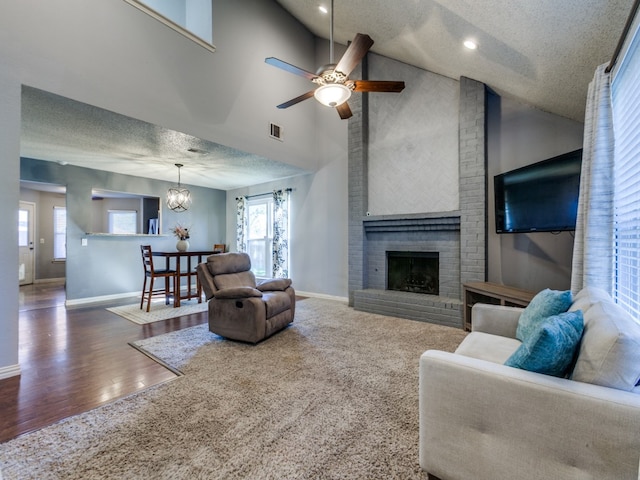 living room with a textured ceiling, ceiling fan with notable chandelier, dark wood-type flooring, high vaulted ceiling, and a fireplace