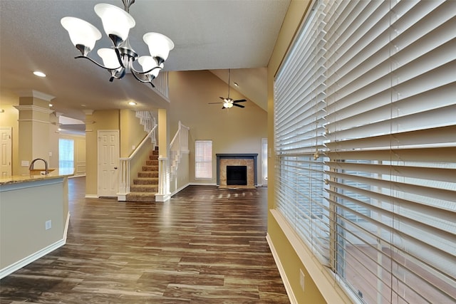 unfurnished living room with vaulted ceiling, a tile fireplace, ceiling fan with notable chandelier, and dark hardwood / wood-style floors