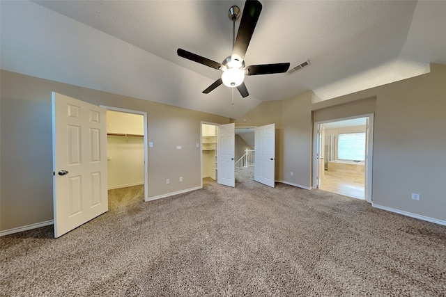 unfurnished bedroom with carpet flooring, a walk in closet, vaulted ceiling, and ceiling fan