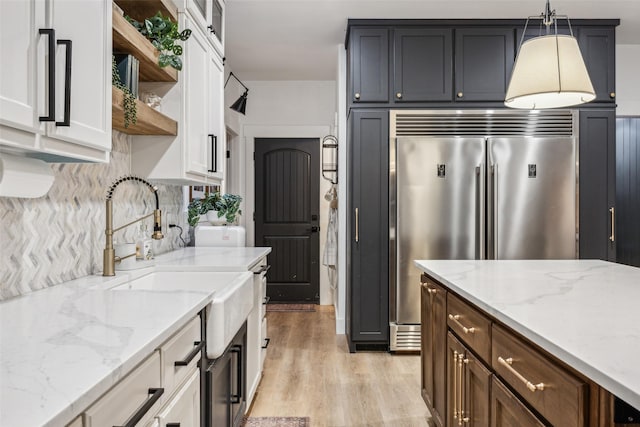 kitchen with built in refrigerator, white cabinets, pendant lighting, and light hardwood / wood-style floors