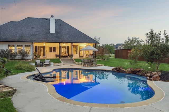 pool at dusk featuring a lawn and a patio area