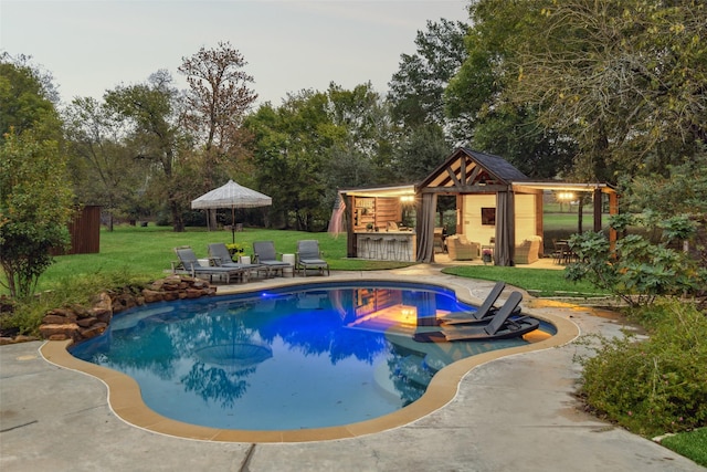 outdoor pool with a patio area, fence, an outdoor structure, a lawn, and outdoor dry bar