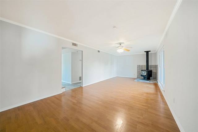 unfurnished living room featuring light wood-type flooring, a wood stove, and crown molding