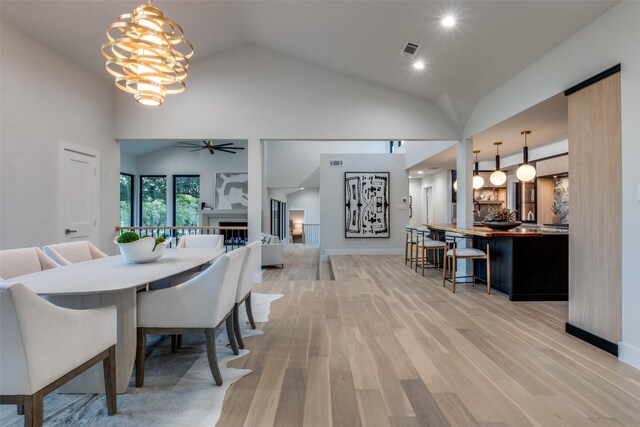 dining area with high vaulted ceiling, light hardwood / wood-style floors, and ceiling fan with notable chandelier