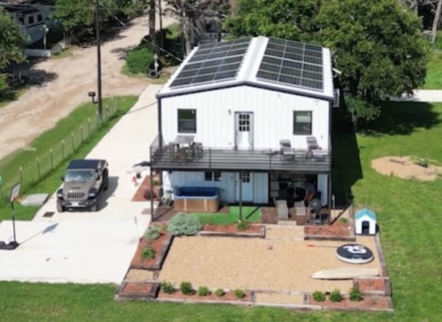 rear view of property featuring a lawn, a hot tub, and solar panels