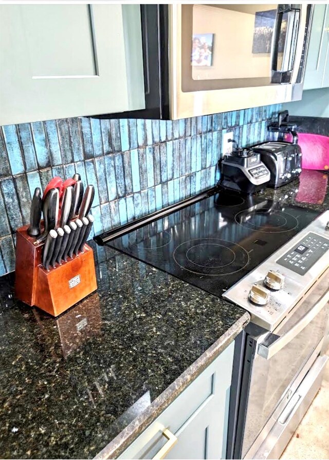 details featuring white cabinets, appliances with stainless steel finishes, decorative backsplash, and dark stone countertops