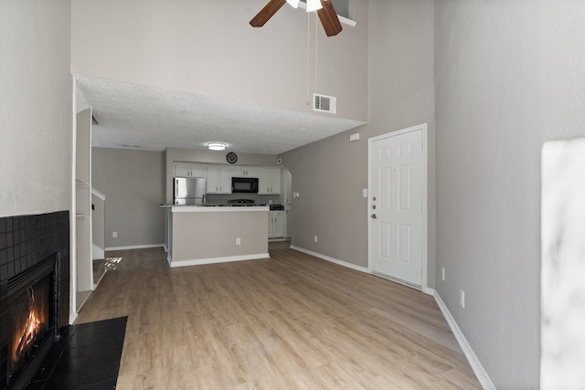 unfurnished living room with a towering ceiling, a textured ceiling, light hardwood / wood-style floors, and ceiling fan