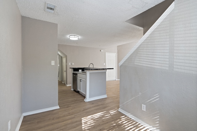 kitchen featuring white cabinets, stainless steel dishwasher, a textured ceiling, and light hardwood / wood-style flooring