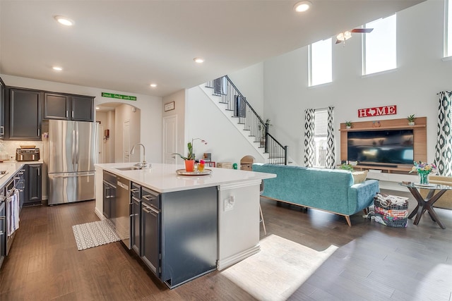 kitchen featuring a center island with sink, sink, a towering ceiling, appliances with stainless steel finishes, and dark hardwood / wood-style flooring