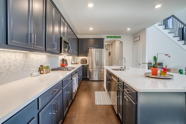 kitchen with tasteful backsplash, stainless steel appliances, a kitchen island with sink, sink, and dark hardwood / wood-style floors