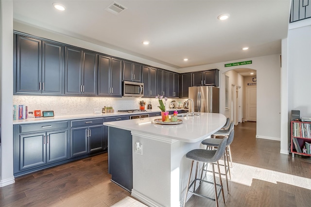 kitchen featuring a kitchen breakfast bar, an island with sink, stainless steel appliances, and dark hardwood / wood-style floors