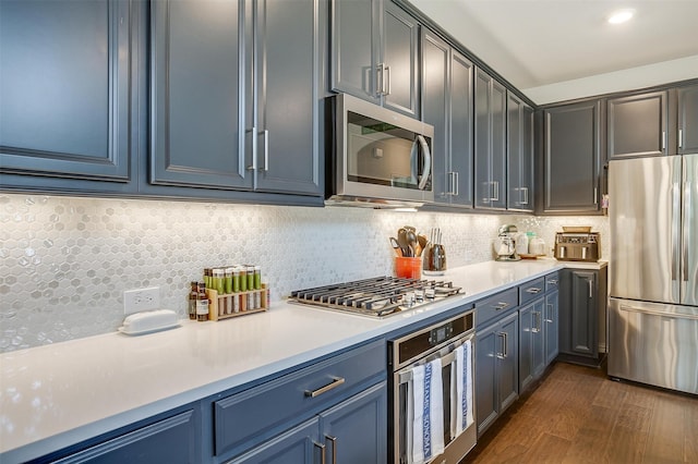 kitchen with backsplash, blue cabinetry, dark wood-type flooring, and stainless steel appliances