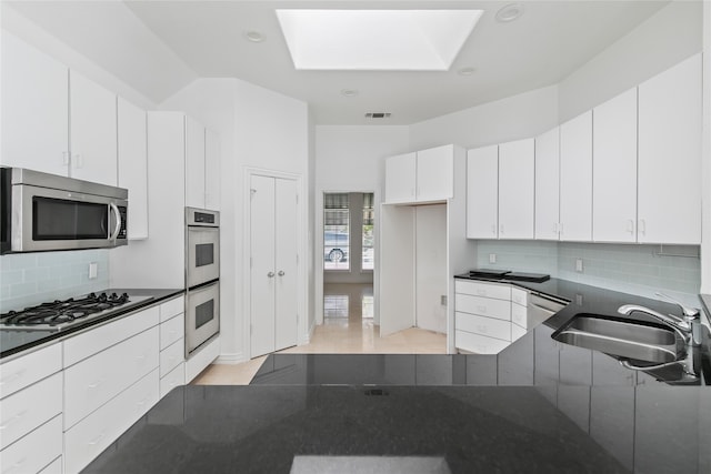 kitchen with backsplash, white cabinets, sink, a skylight, and appliances with stainless steel finishes