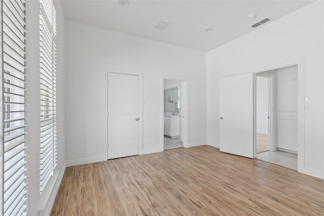 unfurnished bedroom with a closet, light wood-type flooring, and ensuite bath