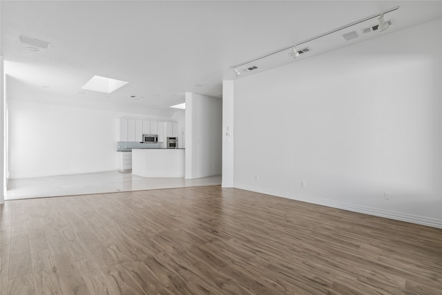 unfurnished living room with a skylight, light hardwood / wood-style floors, and track lighting