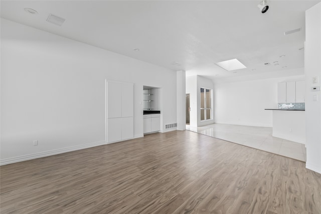 unfurnished living room with light wood-type flooring and a skylight