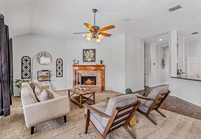 living room with a brick fireplace, a textured ceiling, vaulted ceiling, ceiling fan, and light hardwood / wood-style flooring