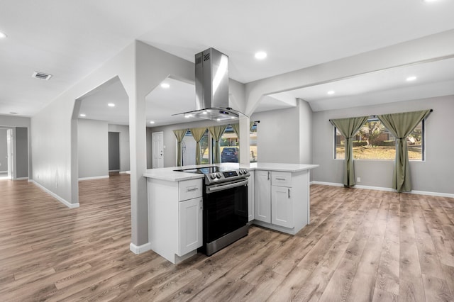 kitchen featuring kitchen peninsula, island range hood, light hardwood / wood-style flooring, white cabinets, and stainless steel electric range