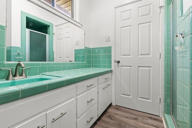 bathroom with wood-type flooring, vanity, a shower with door, and tile walls