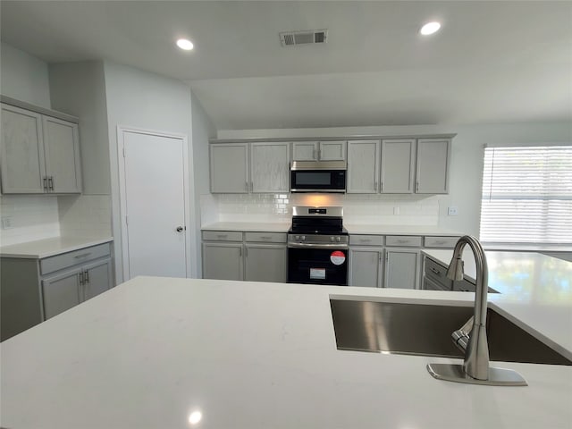 kitchen with gray cabinetry, decorative backsplash, and appliances with stainless steel finishes