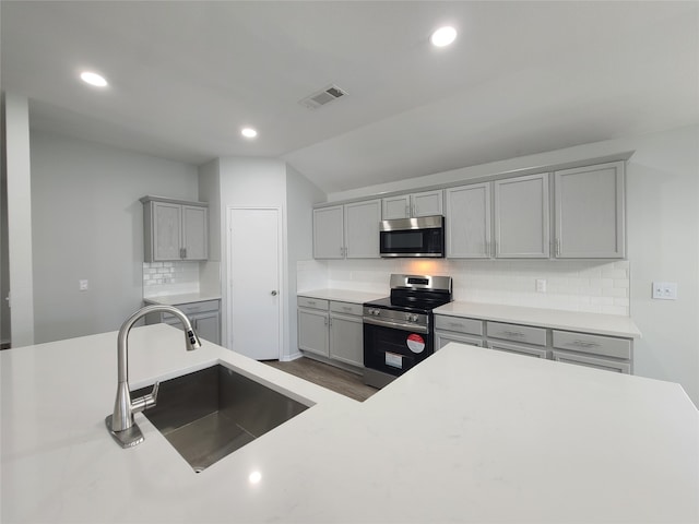 kitchen featuring backsplash, gray cabinetry, stainless steel appliances, vaulted ceiling, and sink