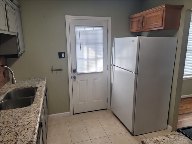 kitchen featuring light stone countertops, sink, white fridge, and light tile patterned floors