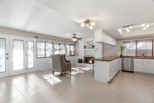 kitchen featuring ceiling fan, stainless steel dishwasher, kitchen peninsula, a fireplace, and white cabinets